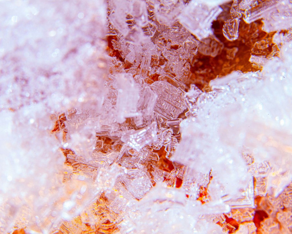 Image is a color photograph of white and red salt crystals; title card for the new flash fiction, “The Girl Who Broke Every Omen,” by Hana Xen.