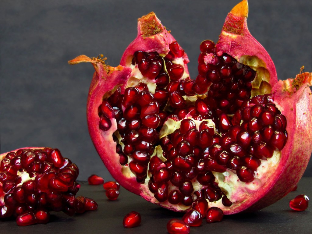 Image is a color photograph of a ripped-open pomegranate; title card for the new microessay, "Red Saturday," by Shira Musicant.