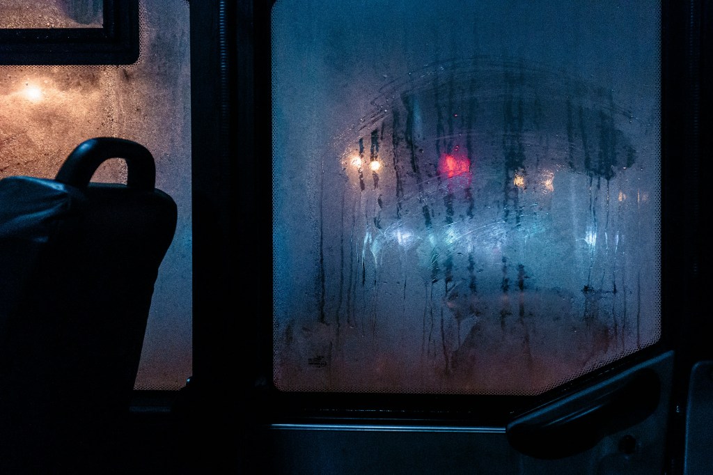 Image is a color photograph of a bus window with condensation at night; title card for the new flash fiction, "The Bus," by Callin Naddy.