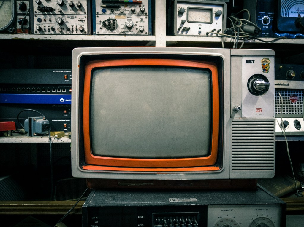 Image is a color photograph of an old television set; title card for "Laid Off from My Own Spin-Off," a new prose poem by Christopher M. Grady.