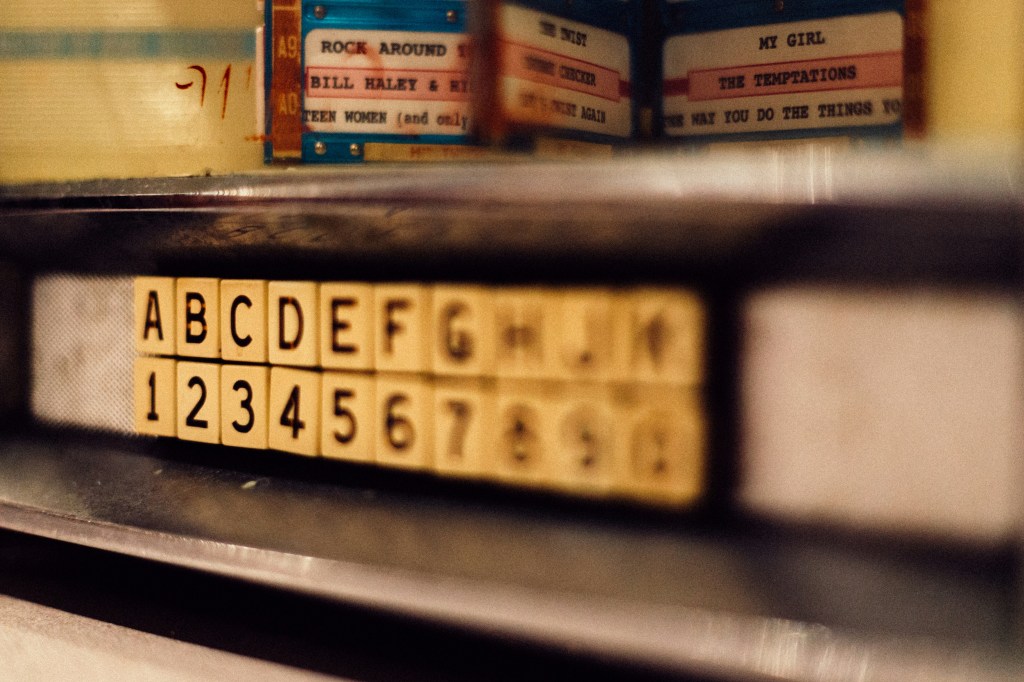 Image is color photograph of an old jukebox; title card for the new microfiction, “Vista Overlooking a Dying Childhood,” by Emily Hoover.