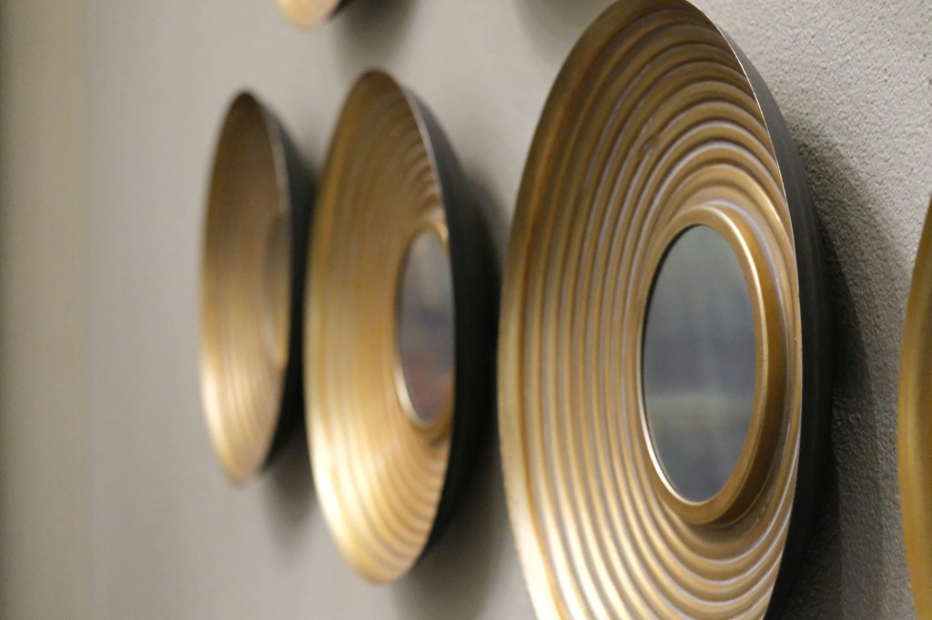 Image is a color photograph of a series of gold-framed mirrors hung on a wall; title card for the new microfiction, "Compromise," by RR Menon.